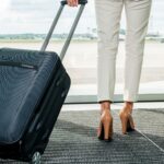 Üzleti útra készülő nő a reptéren várakozik a bőröndjével